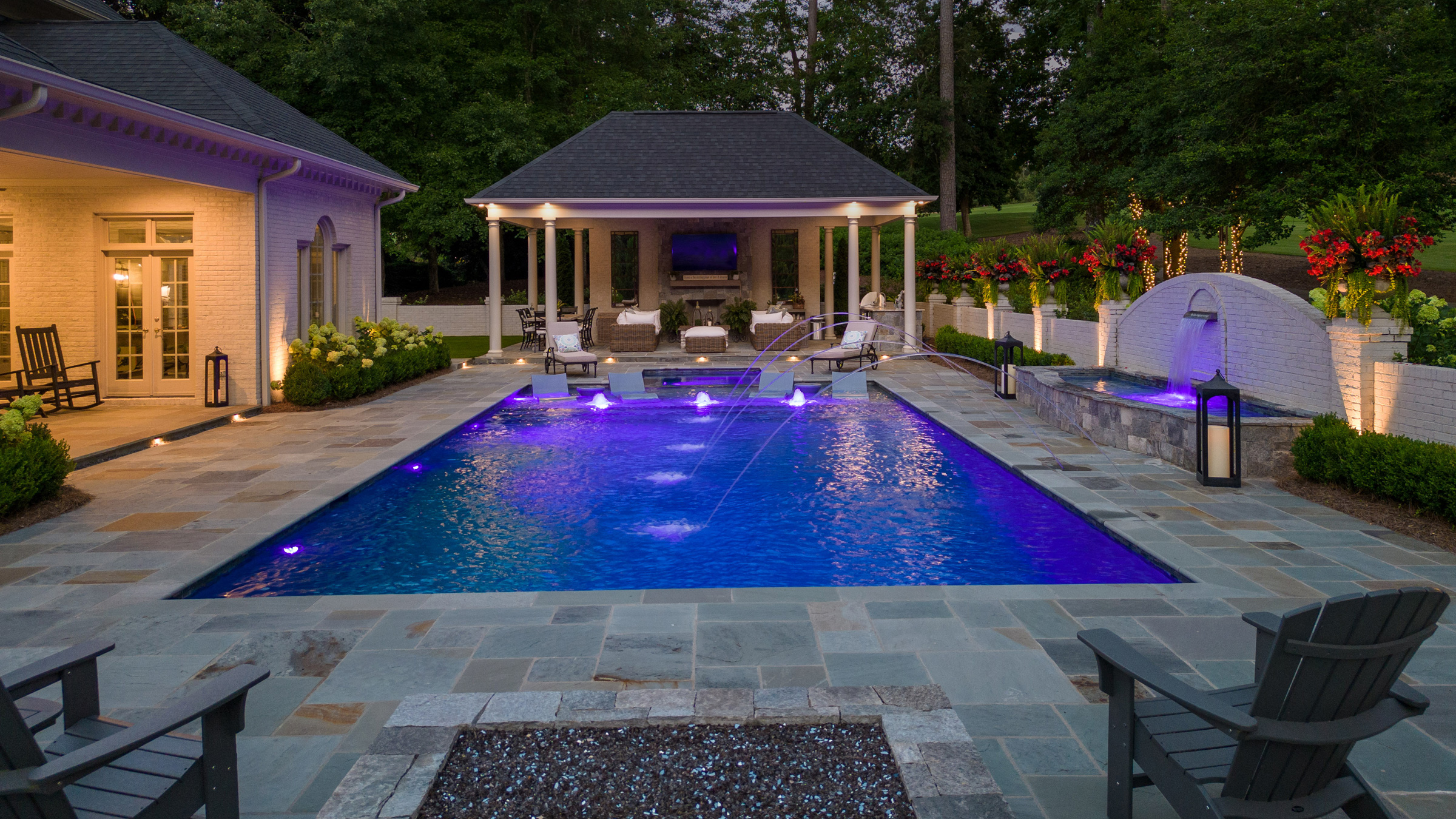 Luxury outdoor pool with illuminated water features, pergola, and elegant pavilion designed by BKF Builders.